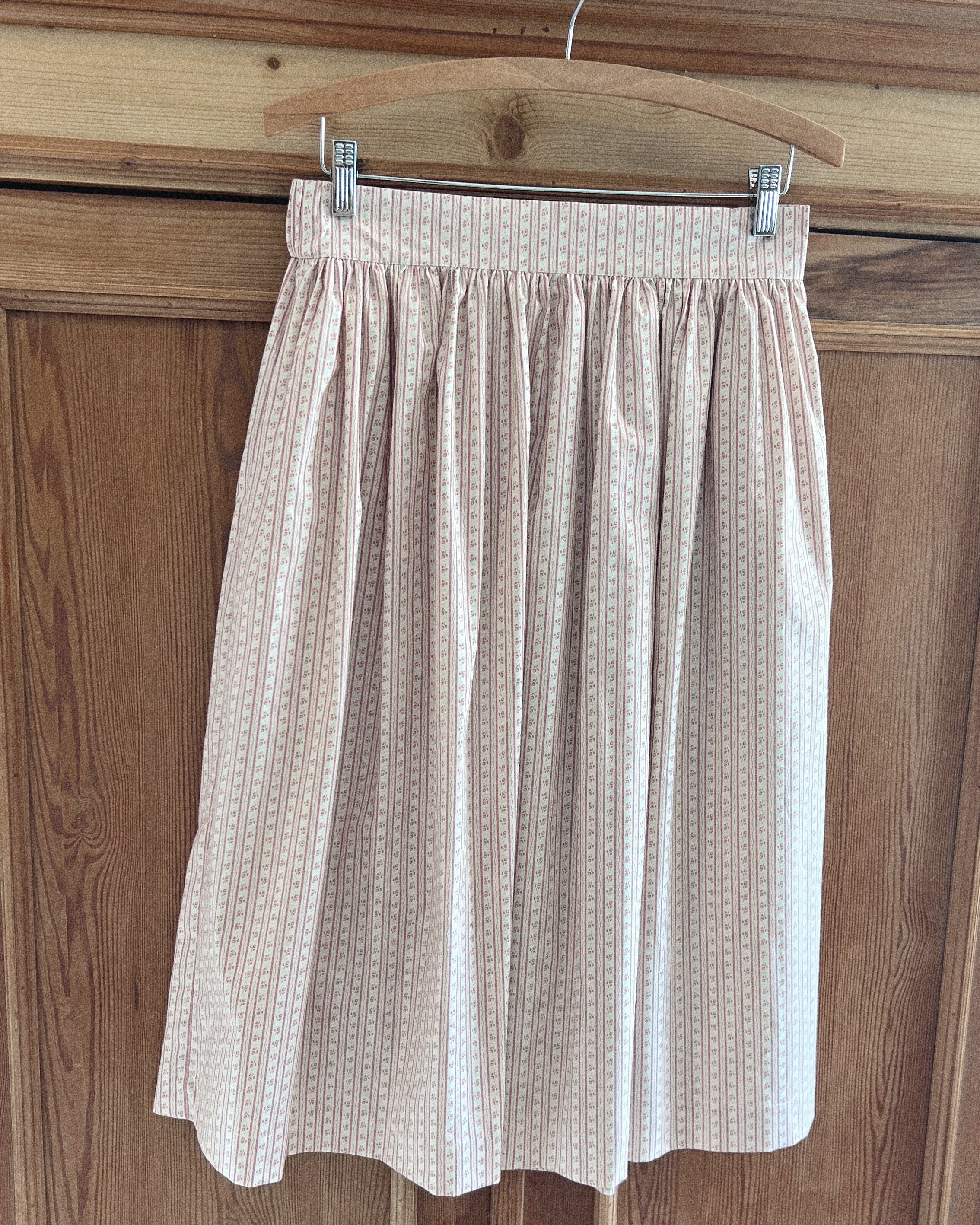 Elle Bohème pure cotton summer midi skirt hanging on a wooden hanger against a wooden panel background