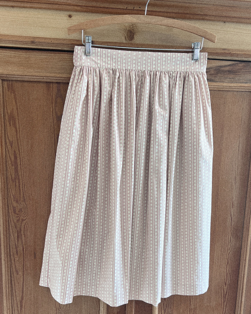 Elle Bohème pure cotton summer midi skirt hanging on a wooden hanger against a wooden panel background