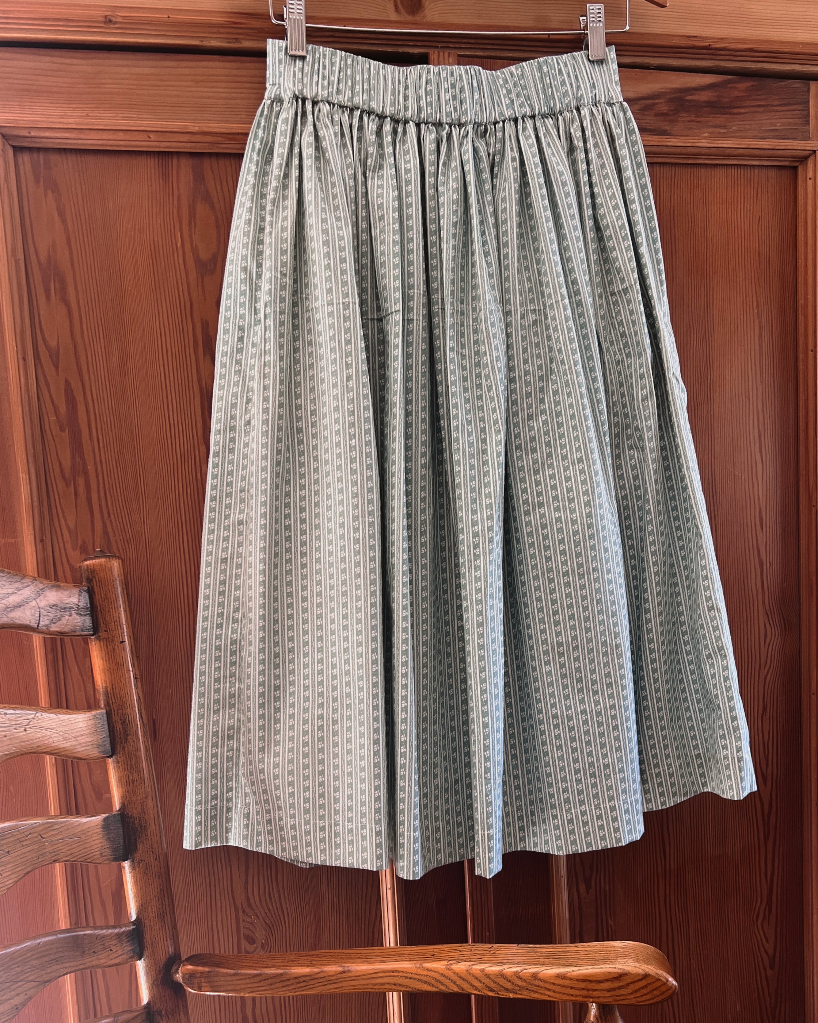 elle boheme pure cotton midi skirt back panel of green patterned skirt hanging on a wooden chair against a wooden wall.