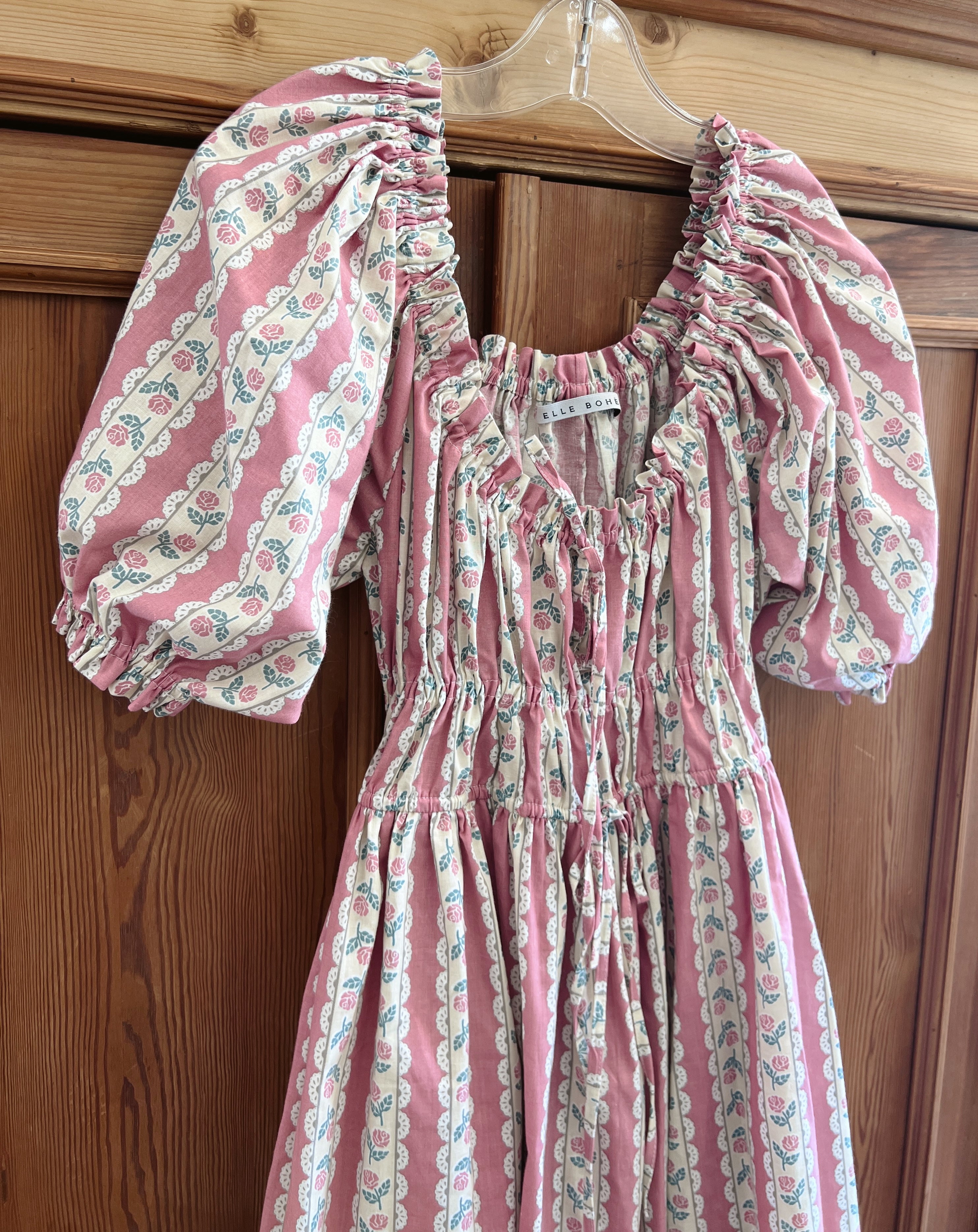 Pink floral dress fabric inspired on vintage wallpaper with puff sleeves and romantic silhouette on a hanger against a wooden background