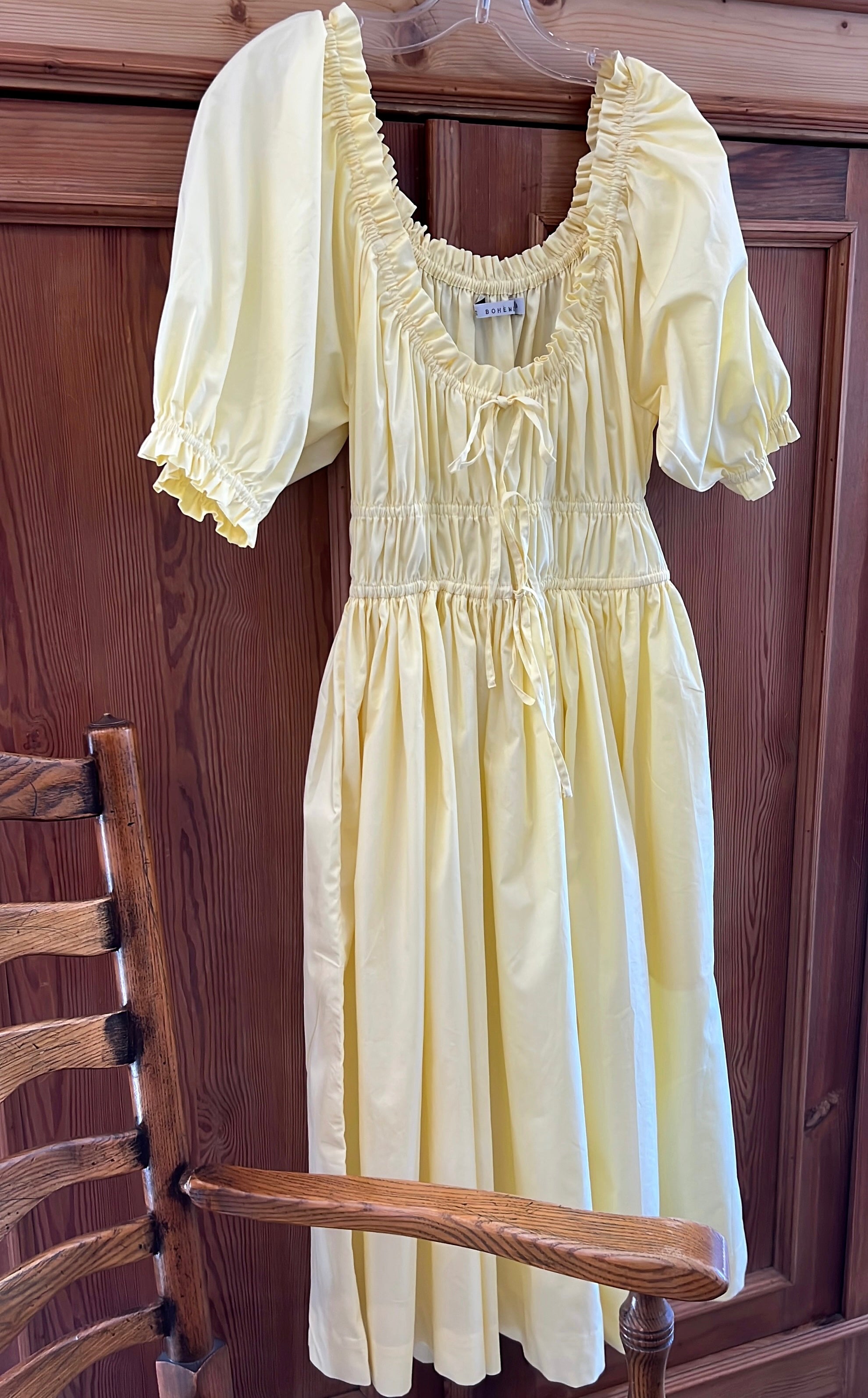 Elle boheme butter yellow colour midi dress hanging from a wooden chair against a wooden background