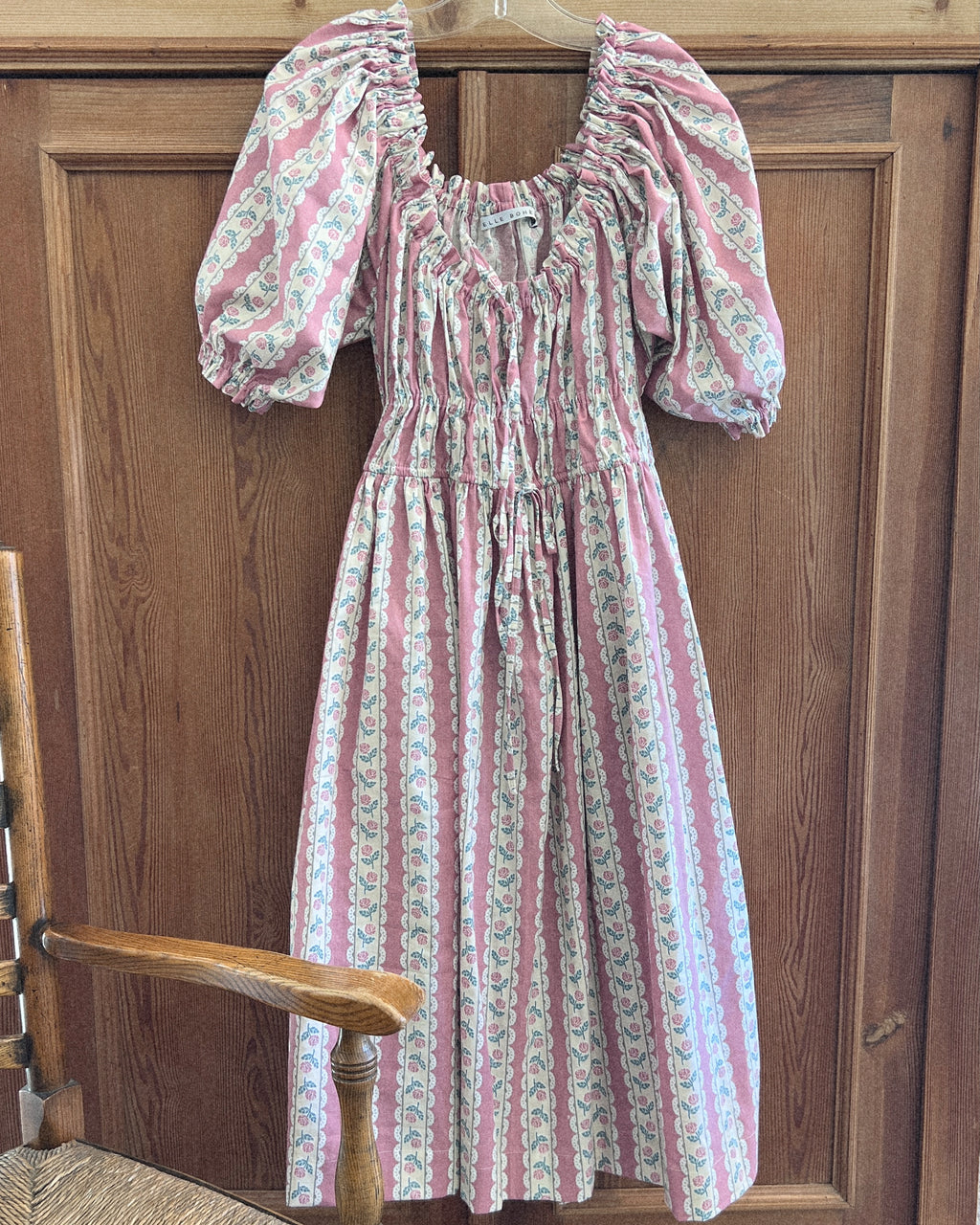 Pink floral dress with puffed sleeves hanging on a wooden door.