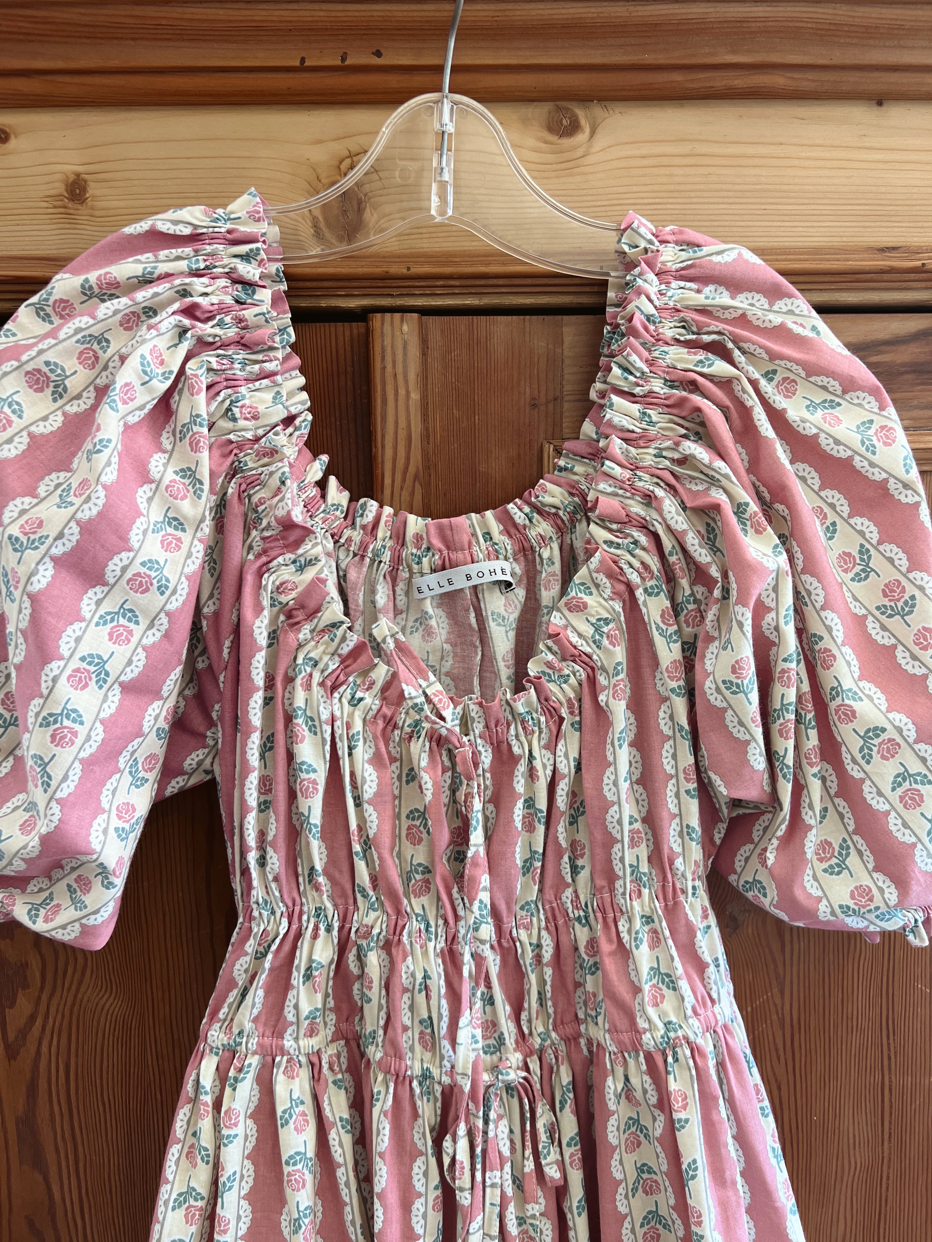 Romantic pink floral dress midi length with puff sleeves on a wooden hanger against a wooden wardrobe