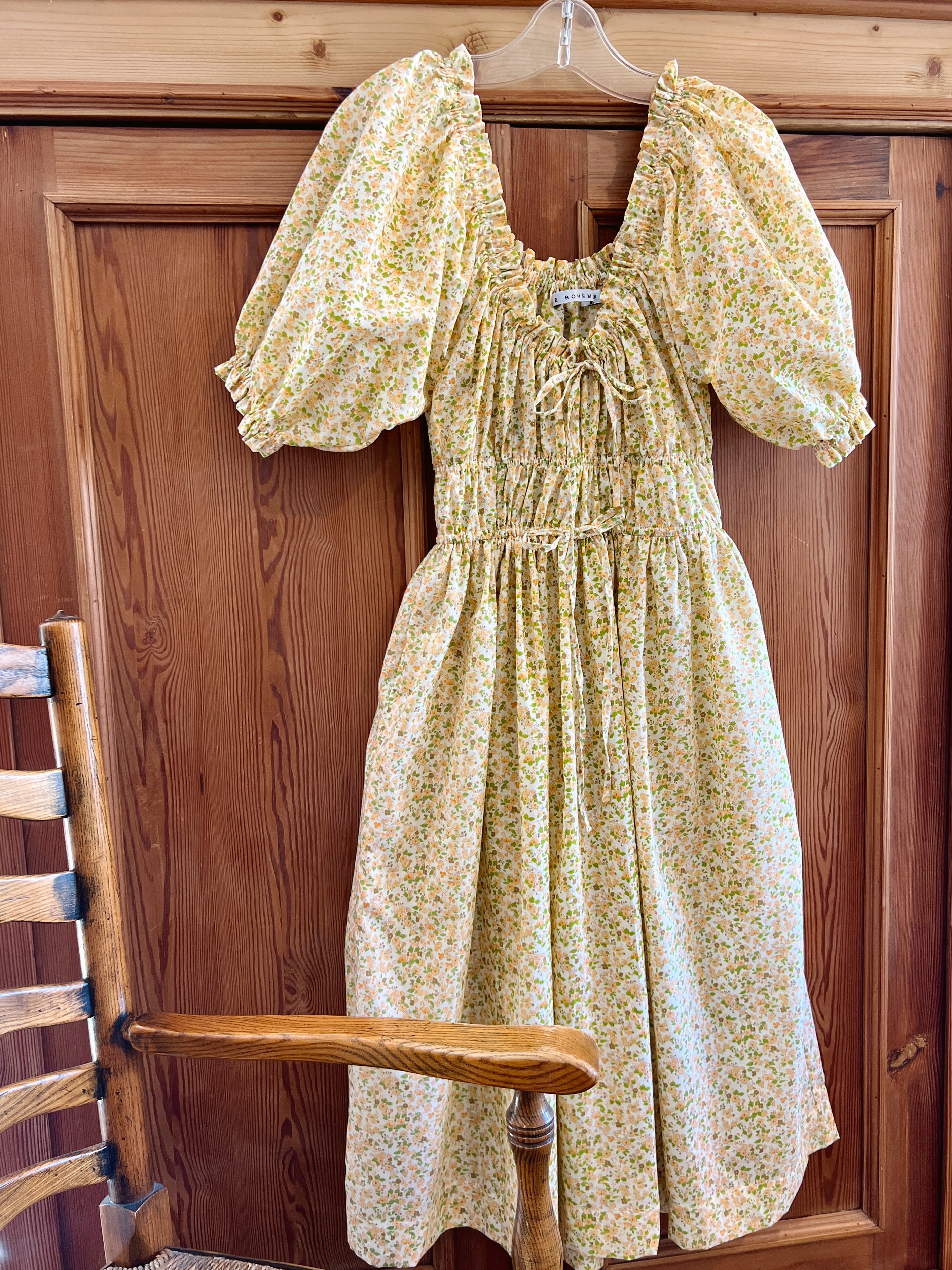 Elle boheme yellow with green accent spring floral dress on a hanger against a pine wooden background