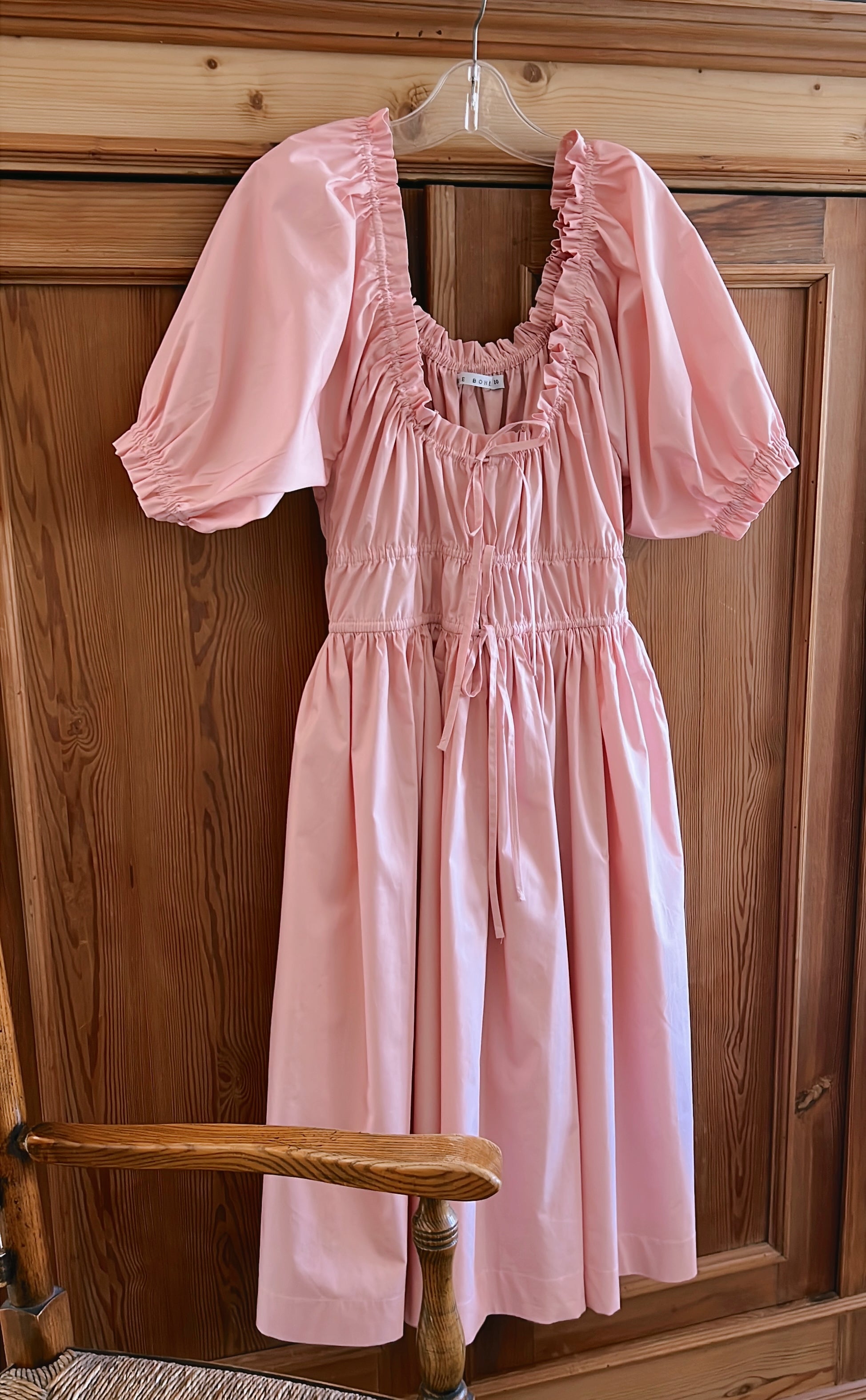 Elle boheme romantic and vintage spring dress made of pure cotton poplin featuring a delicate scoop neckline ruffled sleeves hanging on a cottage wooden door