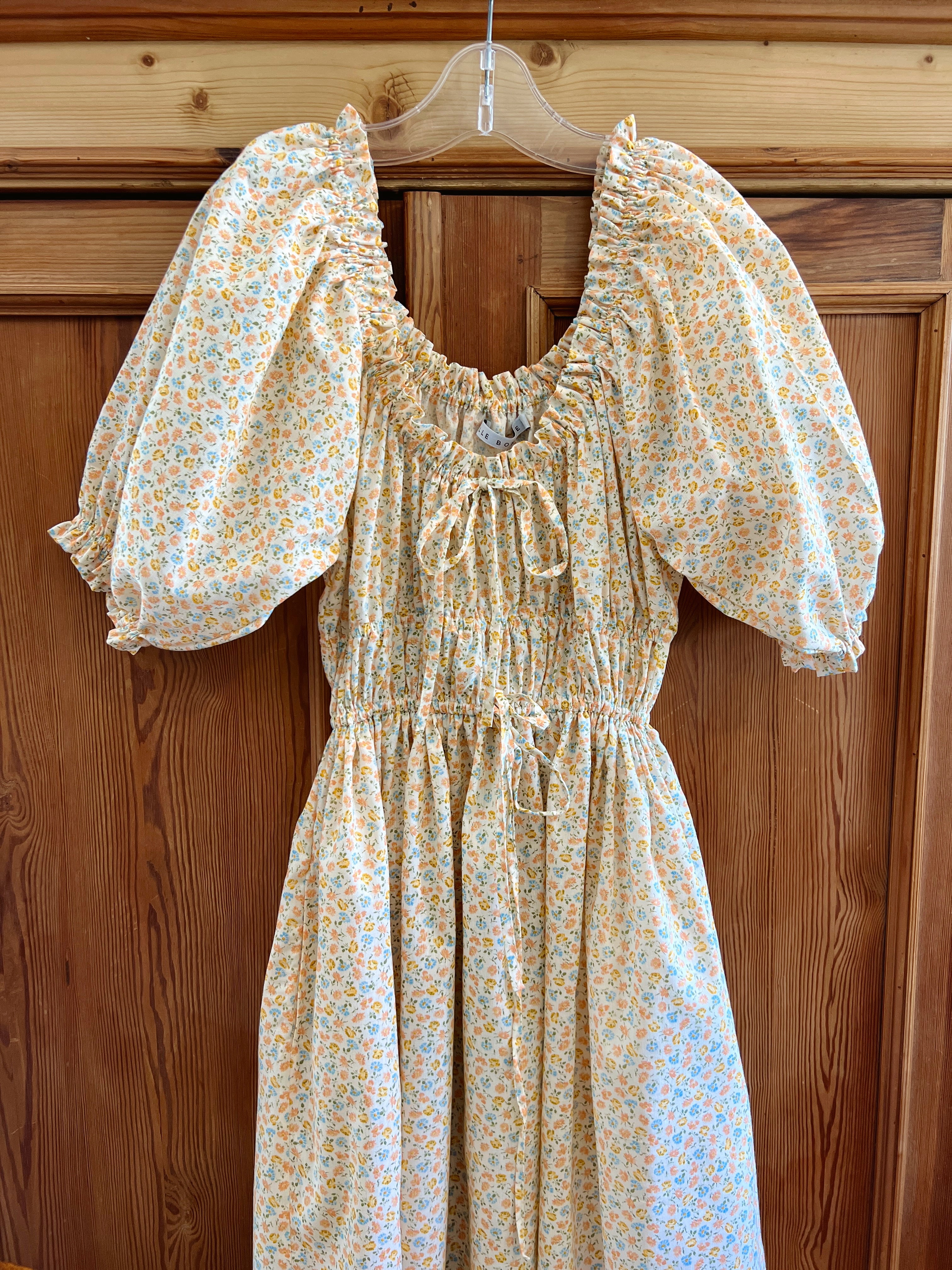 Elle boheme floral midi dress with scoop neckline, puffed sleeves and drawstring hanging on a wooden english pine wardrobe door inside of a British cottage.