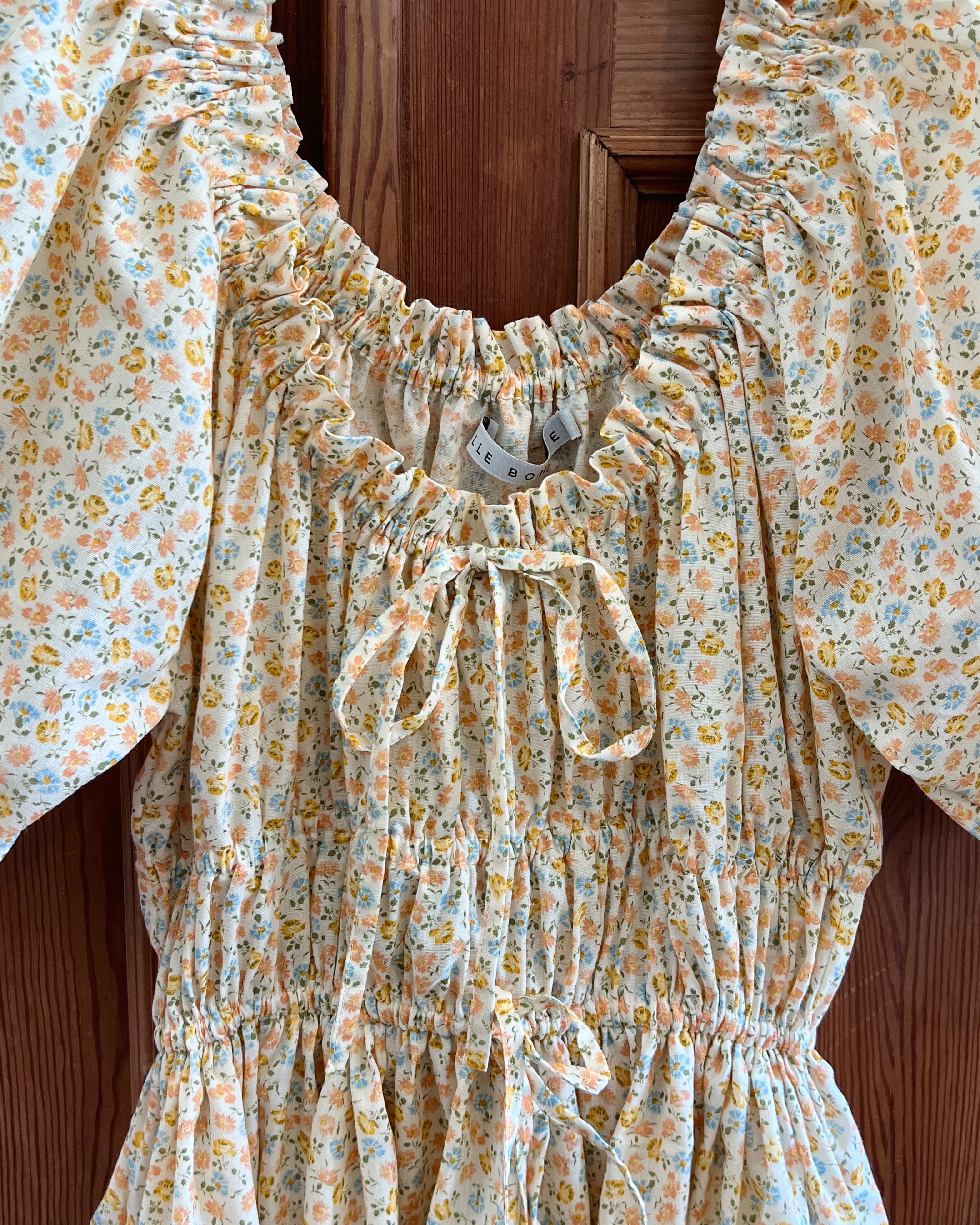 Elle boheme close up romantic floral summer dress with short sleeves and adjustable drawstring waist against a wooden background cottage style.